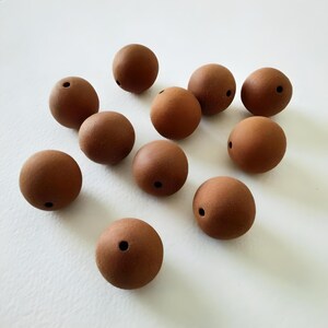 May include: Ten brown wooden beads with a hole in the centre. The beads are round and smooth.