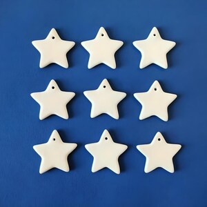 Może przedstawiać: Dziewięć białych ceramicznych ozdób w kształcie gwiazdy z otworem na górze do zawieszenia. Gwiazdy są ułożone w trzy rzędy po trzy na niebieskim tle.
