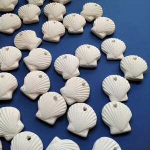 May include: A collection of white ceramic seashells with a heart-shaped cutout in the centre. The seashells are scattered on a blue background.
