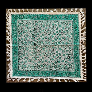 May include: A square green and white cotton tablecloth with a floral pattern and white fringe trim.