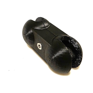 May include: A black, 3D-printed, elongated connector piece with a textured, layered surface. It features two rounded ends with circular indentations and a central metal nut embedded in the side, designed for joining two cylindrical components together.