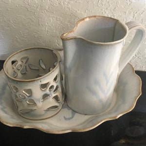 May include: A white ceramic serving set with a pitcher, a decorative candle holder, and a scalloped serving tray. The set has a light blue glaze with a subtle marbled effect.