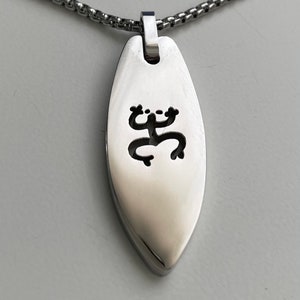 Op de afbeelding: Een zilveren ketting met een zilveren hanger in de vorm van een surfboard met een uitgesneden kikkerontwerp.
