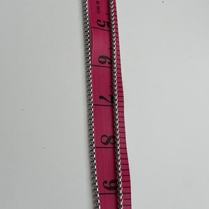 Puede incluir: Un collar de cadena de plata con un colgante redondo que presenta un dise&ntilde;o estilizado. La cadena mide 23 cm de largo y el colgante aproximadamente 2,5 cm de di&aacute;metro. El collar est&aacute; hecho de acero inoxidable.