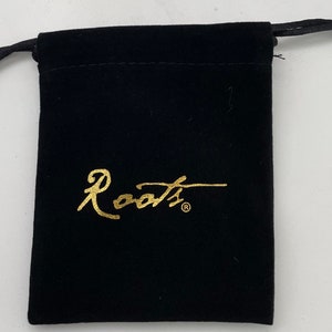 Puede incluir: Una bolsa de cord&oacute;n de terciopelo negro con un logotipo "Roots" dorado.