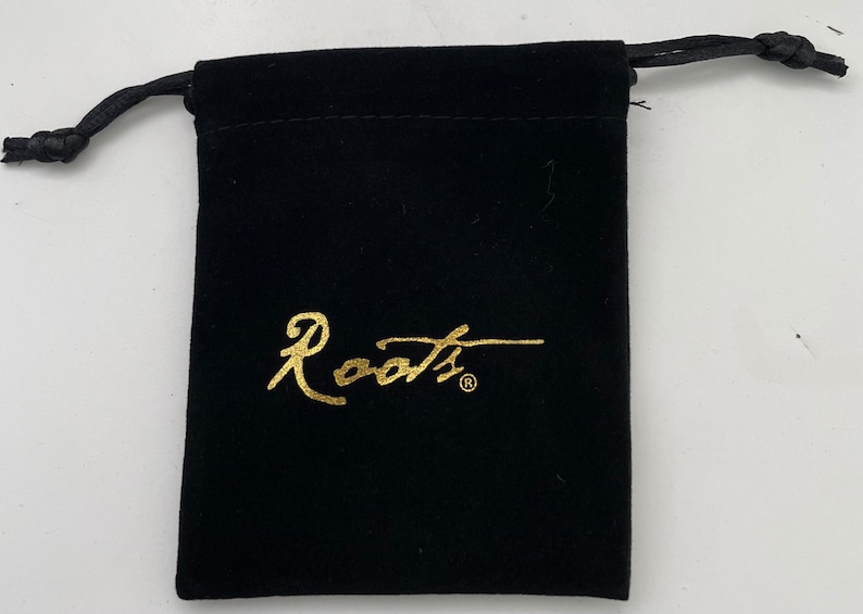 Puede incluir: Una bolsa de cord&oacute;n de terciopelo negro con un logotipo "Roots" dorado.