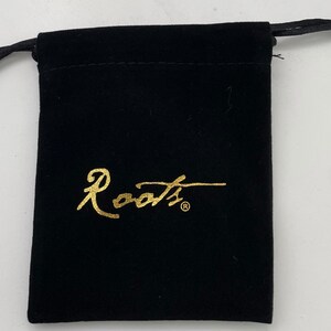 Op de afbeelding: Een zwarte fluwelen trekkoordtas met een gouden "Roots"-logo.