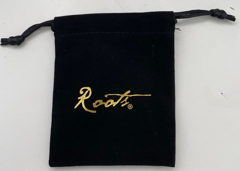Op de afbeelding: Een zwarte fluwelen trekkoordtas met een gouden "Roots"-logo.