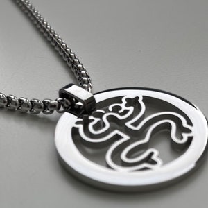 Puede incluir: Un collar de cadena de plata con un colgante redondo que presenta una figura estilizada recortada en el centro.