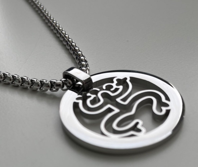 Puede incluir: Un collar de cadena de plata con un colgante redondo que presenta una figura estilizada recortada en el centro.