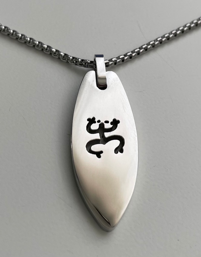 Op de afbeelding: Een zilveren ketting met een zilveren hanger in de vorm van een surfboard met een uitgesneden kikkerontwerp.