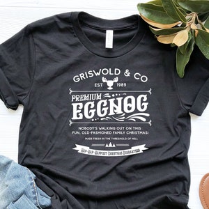May include: Black t-shirt with white text that reads "Griswold & Co. Est 1989 Premium Eggnog. Nobody's walking out on this fun, old-fashioned family Christmas! Made fresh in the threshold of hell.  Snap Snap Happiest Christmas Guarantee."