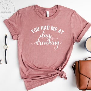 May include: A pink t-shirt with the text "You had me at day drinking" in white lettering.