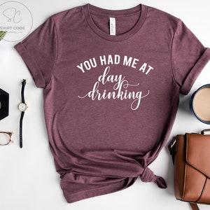 May include: A maroon t-shirt with the text "You had me at day drinking" in white.