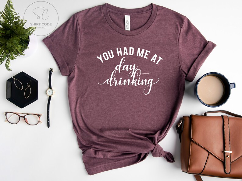 May include: A maroon t-shirt with the text "You had me at day drinking" in white.