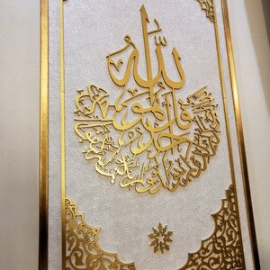 May include: A gold framed wall art piece with intricate Islamic calligraphy in a white background. The calligraphy is in Arabic and reads "Allah" in the center.