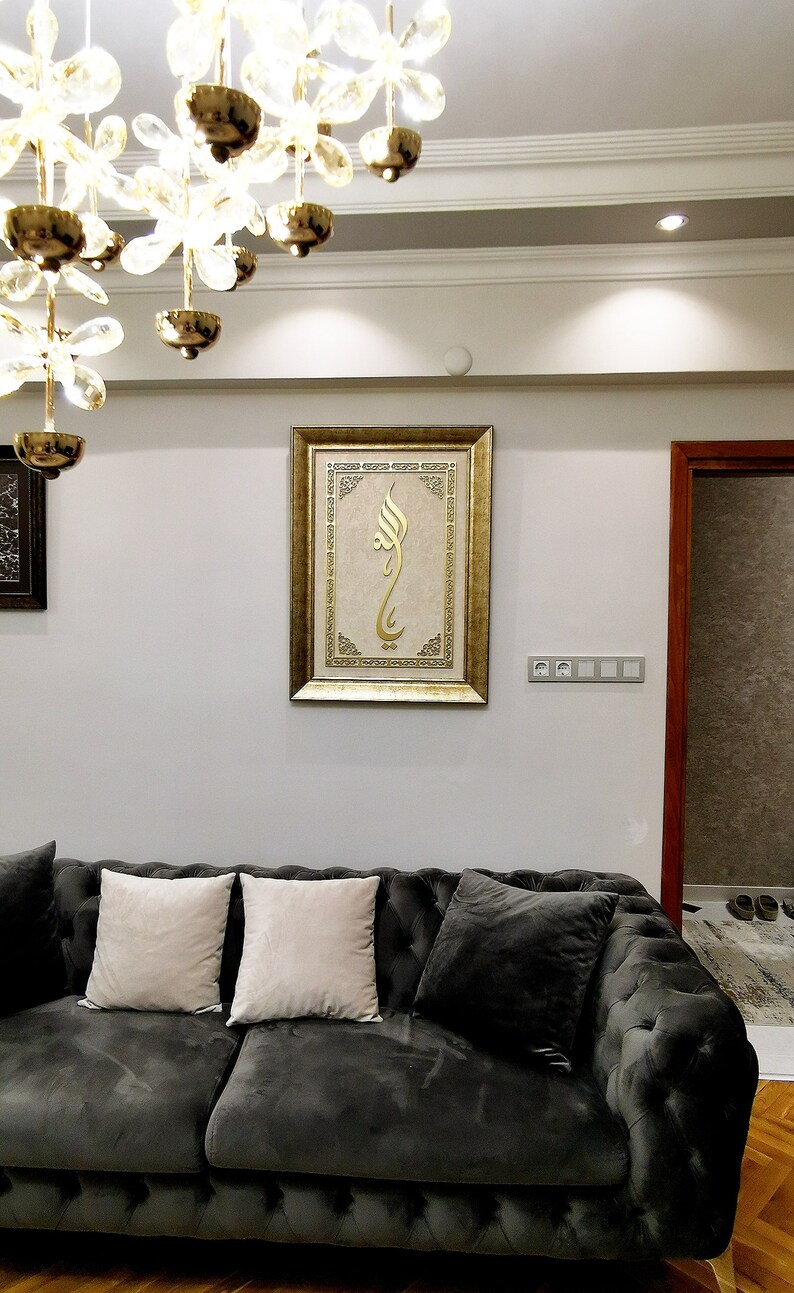 K&ouml;nnte beinhalten: Ein dunkelgraues Samtsofa mit zwei wei&szlig;en Kissen und einem goldgerahmten Bild mit islamischer Kalligraphie, das an der Wand dahinter h&auml;ngt.