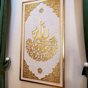 May include: A gold framed wall art piece with intricate cut-out designs. The center features a large Arabic calligraphy inscription in gold.