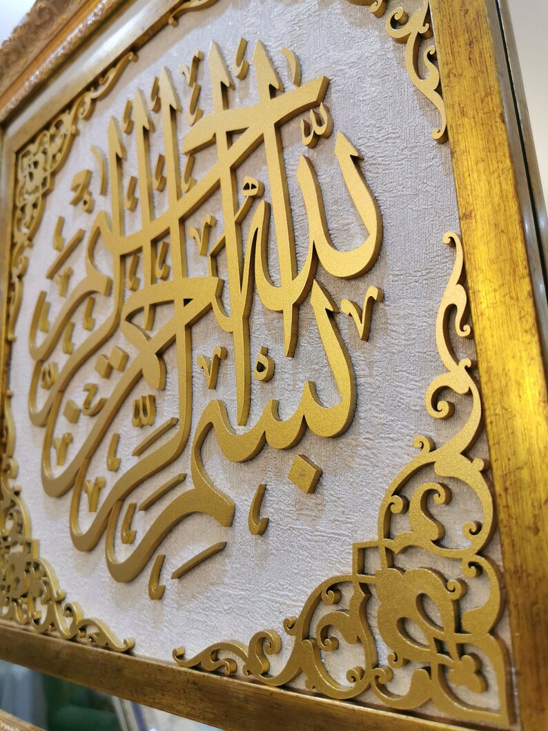 May include: A gold framed wall art piece with intricate carvings. The center of the art piece features a raised, gold Arabic calligraphy inscription.