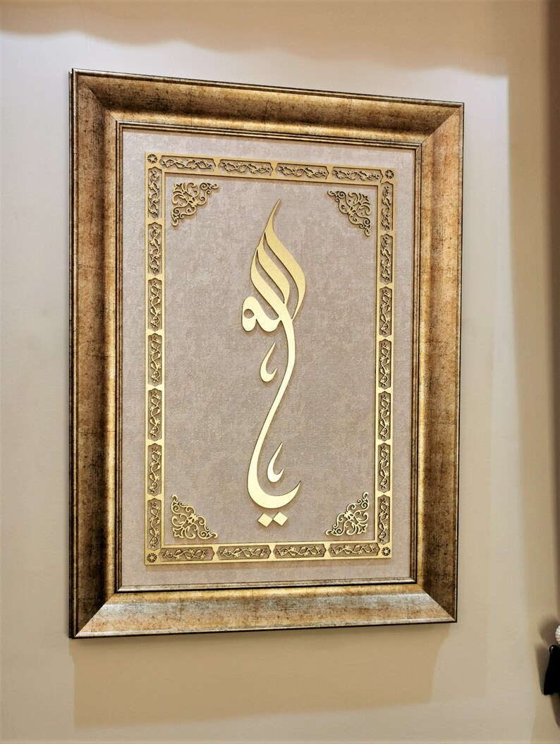 K&ouml;nnte beinhalten: Ein gerahmtes St&uuml;ck islamischer Kalligrafiekunst mit goldenen Buchstaben auf beigefarbenem Hintergrund. Der Rahmen ist verziert und hat eine goldene Oberfl&auml;che.