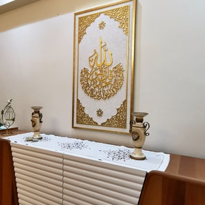 May include: A white dresser with a gold-colored frame with intricate designs and Arabic calligraphy. Two gold-colored vases are on top of the dresser.