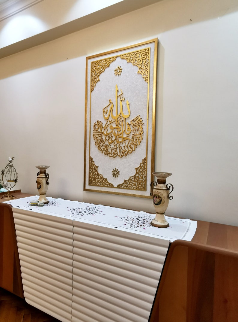 May include: A white dresser with a gold-colored frame with intricate designs and Arabic calligraphy. Two gold-colored vases are on top of the dresser.