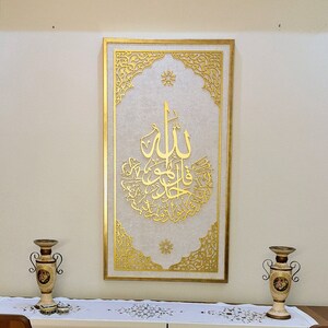 May include: A gold framed wall art piece with intricate designs and Arabic calligraphy. The background is white with a subtle texture.