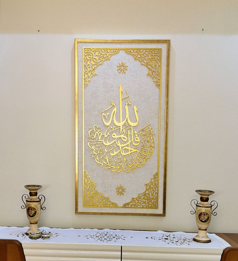 May include: A gold framed wall art piece with intricate designs and Arabic calligraphy. The background is white with a subtle texture.