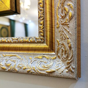 May include: Close-up of a gold and white ornate picture frame with a decorative floral design. The frame is made of wood and has a distressed finish.