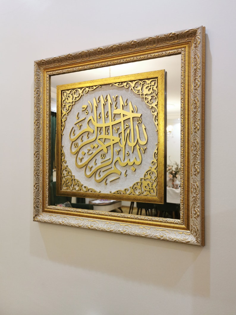 May include: A gold framed mirror with a white background and gold calligraphy inside. The calligraphy is in Arabic and reads "Allah".