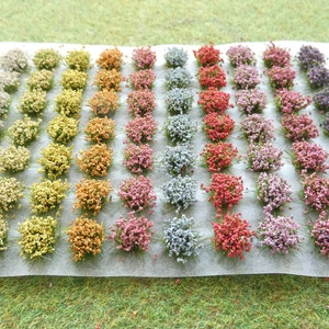 May include: A sheet of white paper with 40 small clusters of artificial flowers in various colours, including white, yellow, orange, pink, red, purple, and blue. The flowers are arranged in rows, creating a gradient effect.
