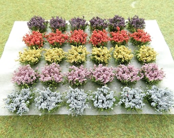 Puede incluir: Un conjunto de 36 racimos de flores artificiales en varios colores, incluyendo morado, rojo, amarillo, rosa y azul. Los racimos están dispuestos en filas sobre una superficie blanca.