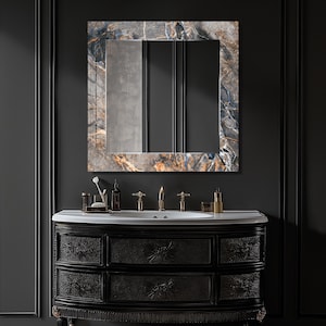 May include: A rectangular bathroom mirror with a marble-like frame in shades of blue, brown, and gray hangs above a black vanity. The vanity has floral carvings on the drawers and a white countertop. Gold fixtures and accessories are visible.