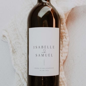 May include: A white wine bottle label with the text "Isabelle & Samuel" and the date "15.09.2022" with the words "Cheers to love & happiness".