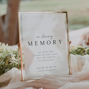 May include: A gold-framed sign with the words "in loving memory" in black script. The sign includes text about those who are missed, and the names Ellie & Ryan, with a date. The sign is on a draped surface.