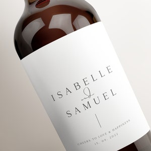 May include: A white wine bottle label with the text "Isabelle and Samuel" and "Cheers to love & happiness 15.09.2022".