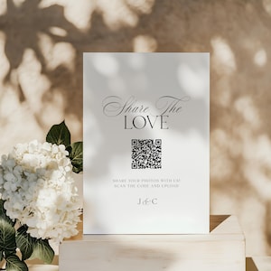 Könnte beinhalten: Ein weißes Schild mit dem Text "Share The LOVE" in eleganter Schrift, einem QR-Code und dem Text "SHARE YOUR PHOTOS WITH US! SCAN THE CODE AND UPLOAD". Ein Strauß weißer Blumen befindet sich im Vordergrund.