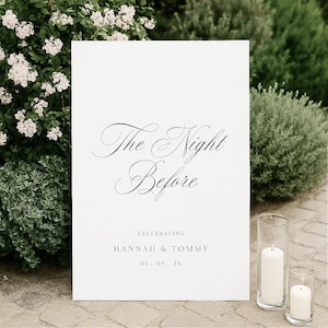 May include: A rectangular white sign with black text that reads The Night Before, followed by CELEBRATING HANNAH & TOMMY and the date 05 . 09 . 2X. The sign features elegant script lettering for the main title and simple sans-serif font below.
