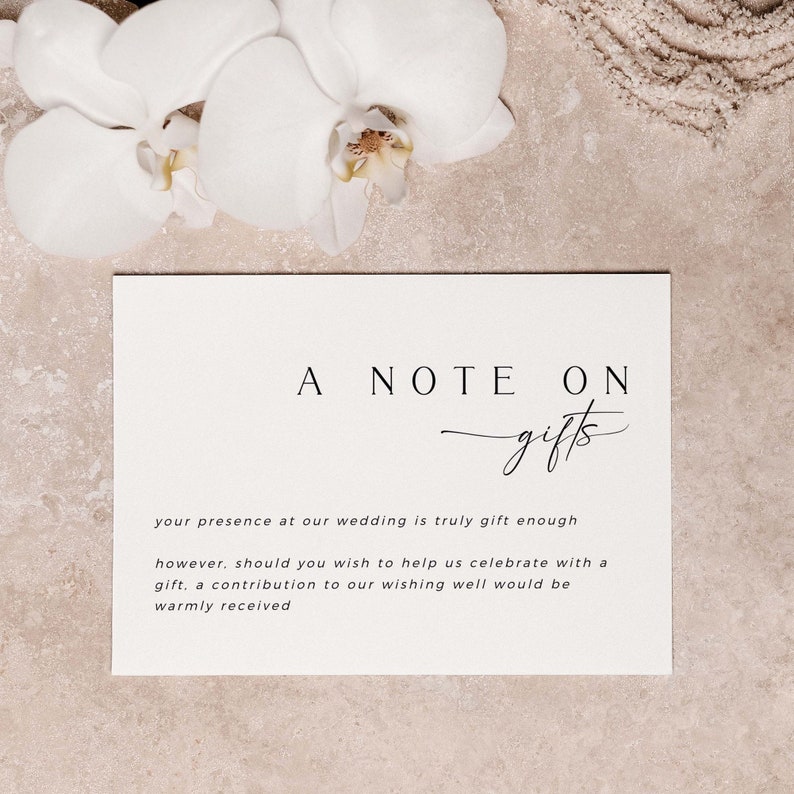 Op de afbeelding: Een witte kaart met zwarte tekst die "A Note On Gifts" luidt. De tekst gaat verder: "Uw aanwezigheid op onze bruiloft is al een cadeau op zich, maar mocht u ons willen helpen met het vieren van onze dag met een cadeau, dan is een bijdrage in onze wensfontein van harte welkom."