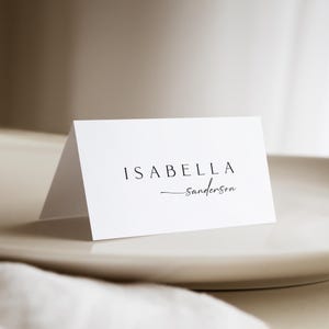 Peut inclure: Carte de table blanche avec le nom "Isabella Sanderson" &eacute;crit en noir.