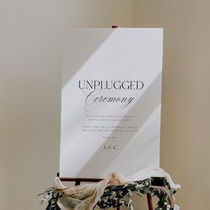 May include: A white sign with the words "UNPLUGGED Ceremony" in elegant black script. The sign also includes the text "We invite you to be fully present with us during our ceremony. Kindly turn off all phones & cameras and enjoy this special moment with us. Thank you. J&C."