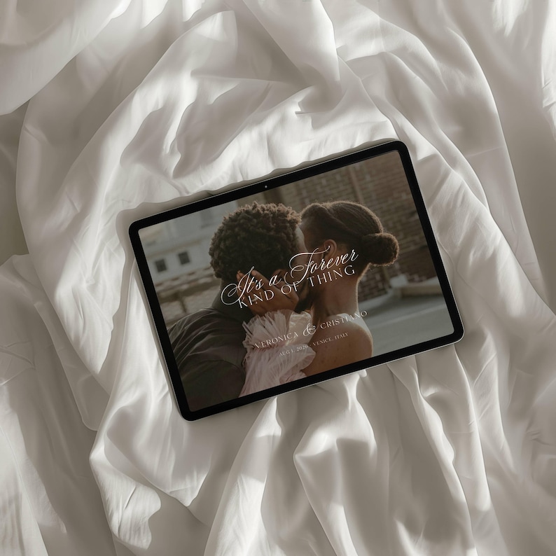 K&ouml;nnte beinhalten: Ein Tablet zeigt eine Hochzeitseinladung mit dem Text "It's a Forever Kind of Thing". Die Einladung zeigt ein Foto eines sich k&uuml;ssenden Paares. Das Tablet liegt auf einem wei&szlig;en, strukturierten Stoff.