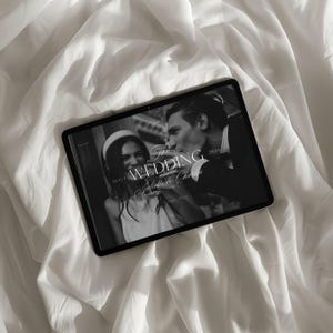 May include: A black and white image of a tablet displaying a wedding photo. The tablet is on a white, textured surface. The photo features a couple, with the text "The Wedding" and names. The date "2026" is also visible.