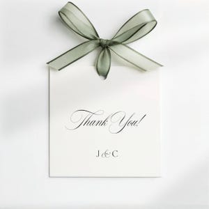 May include: A white rectangular gift tag with the words "Thank You!" in elegant script, topped with a sage green sheer ribbon bow. The tag also includes the initials "J & C" in a smaller font.