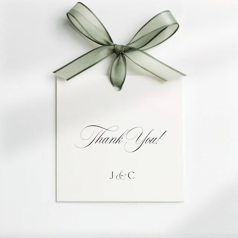 May include: A white rectangular gift tag with the words "Thank You!" in elegant script, topped with a sage green sheer ribbon bow. The tag also includes the initials "J & C" in a smaller font.