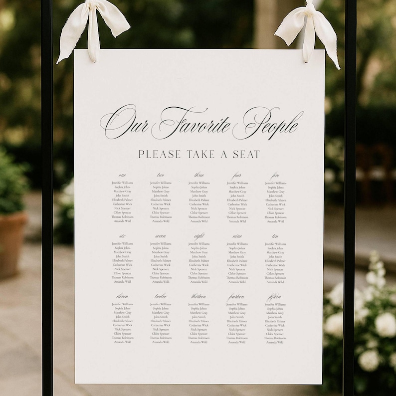 May include: A white seating chart with the text "Our Favorite People" and "Please Take a Seat" in elegant script. The chart is divided into columns with guest names. White ribbons are tied at the top for hanging. The overall theme is a wedding or event.
