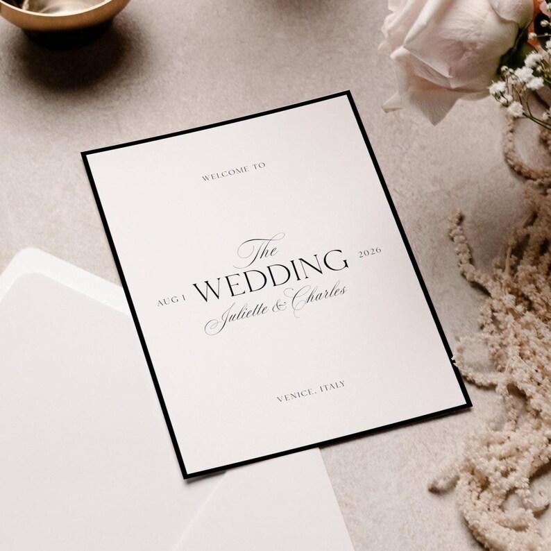 Pu&ograve; includere: Un invito di nozze bianco con bordo nero. Il testo recita "Welcome to The Wedding Juliette & Charles 2020" e "Venice, Italy". Una busta bianca &egrave; visibile in basso a sinistra.