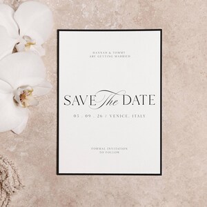 May include: A formal wedding invitation with a black border. The text reads "HANNAH & TOMMY ARE GETTING MARRIED" and "SAVE THE DATE" in elegant script. The date is 03.09.26 in Venice, Italy. White orchids are in the background.