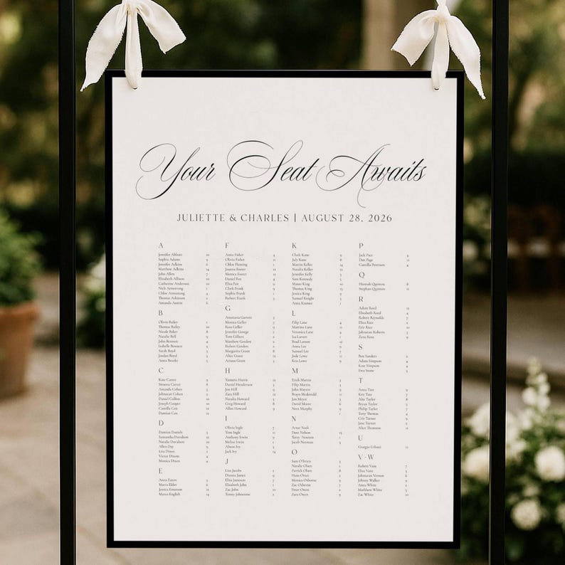 May include: A wedding seating chart with the words "Your Seat Awaits" in elegant script. The names of the guests are listed alphabetically. The chart is framed in black and adorned with white ribbons.