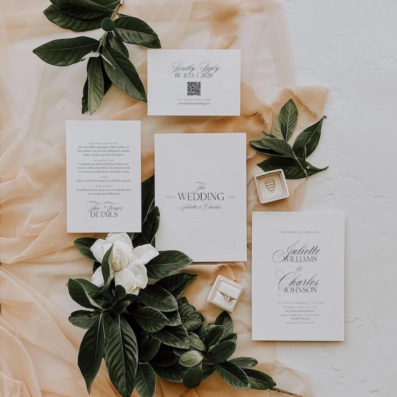 May include: A sophisticated wedding invitation set, comprising white cards with black lettering. The set includes information, reply, and invitation cards, a ring box, and floral decorations. The text includes "The Wedding" and names.